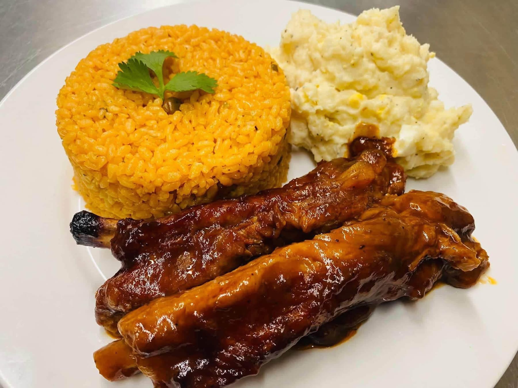Sauced chicken with yellow rice and a side of potato salad